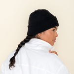Black Golightly Cashmere Watchcap being worn by a person with a long dark braid, seen from a side profile. 