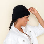 Black Golightly Cashmere Watchcap being worn by a person with a long dark braid, seen from a side profile. 