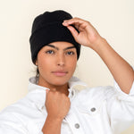 A person wearing a black, 6-ply ribbed knit cashmere watchcap, paired with a white denim jacket.