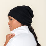 Side profile of a person wearing a black, 6-ply ribbed knit cashmere watchcap, paired with a white jacket and featuring a long, dark braid.